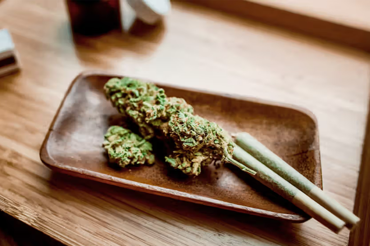 Cannabis flower and pre-rolled joints on wooden serving tray